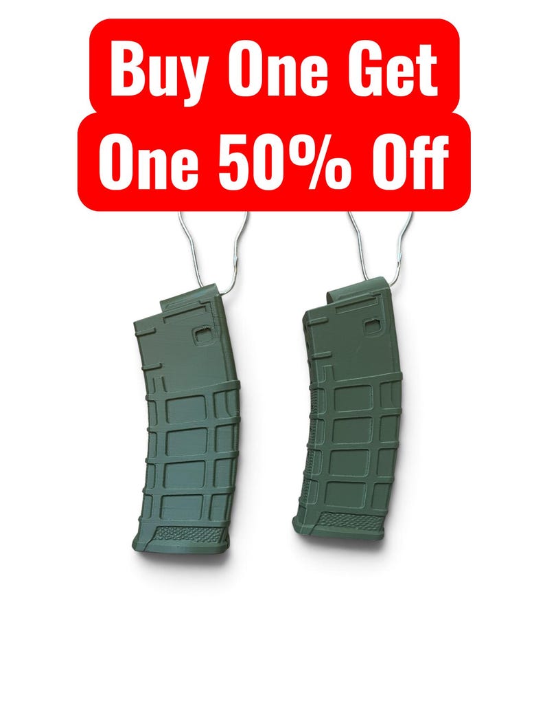 May include: Two olive green polymer rifle magazines with a textured grid pattern on the exterior, each suspended by a silver metal hook. Above the magazines, a red rectangular sign displays the white text Buy One Get One 50% Off.