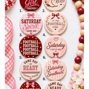 May include: A collection of ten circular buttons featuring football-themed designs in shades of red, pink, and cream. Each button displays unique text such as Gameday Girl, Saturday Spirit, and Football Era, accented with illustrations of bows, boots, and hearts.