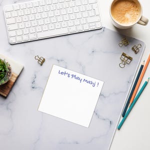 May include: A white keyboard, coffee cup, and pencils are arranged on a marble-patterned desk mat. A small succulent plant sits on a wooden board. A white notepad with the text "Let's Play Mahj!" is in the center.