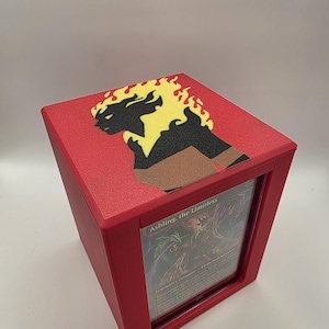 May include: Red card storage box with a framed window. The top of the box features a black and yellow graphic design. The card in the window reads "Ashling, the Limitless".