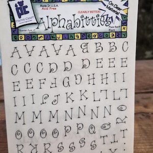 May include: A rectangular sheet of clear material featuring black printed letters in a serif font titled Alphabitties. The sheet includes multiple rows of uppercase and lowercase letters, along with a Provo Craft logo and product information text.