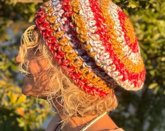 May include: A handmade, colorful crochet hat in shades of red, yellow, and white. The hat is a thick, warm beanie style, perfect for cold weather. The yarn appears to be a chunky weight, giving the hat a textured appearance.