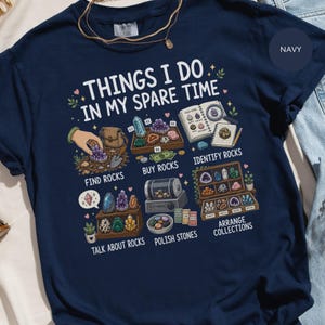 May include: A navy blue t-shirt featuring a graphic print titled THINGS I DO IN MY SPARE TIME. The design illustrates various rock collecting activities including finding, buying, identifying, talking about, polishing, and arranging rocks with labels.