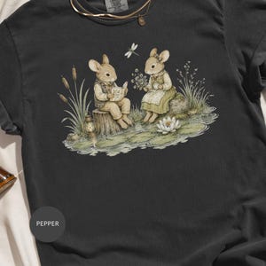 Two mice sit by a pond; one reads a book, the other holds flowers and tea.