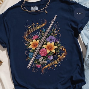 Peut inclure: T-shirt bleu marine avec un motif de flûte argentée entourée de fleurs et de notes de musique. L'arrangement floral comprend des lys jaunes, des roses roses et des hortensias violets. Le texte "COMFORT COLORS" est visible en haut du t-shirt.