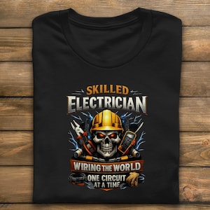 May include: Black t-shirt featuring a skull wearing a yellow hard hat, with tools and lightning bolts. The text reads "SKILLED ELECTRICIAN" above and "WIRING THE WORLD ONE CIRCUIT AT A TIME" below the skull graphic.