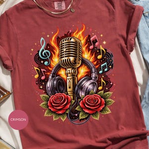 Puede incluir: Camiseta de color carmesí con un diseño gráfico de un micrófono, auriculares, rosas, notas musicales y llamas. El diseño incluye un micrófono dorado, auriculares negros y rosas rojas. La camiseta tiene cuello redondo y mangas cortas.