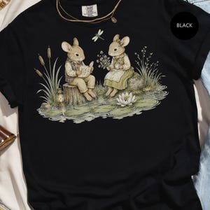 Watercolor illustration of two mice reading and drinking tea by a pond with a dragonfly.