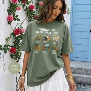 May include: A moss green short-sleeve t-shirt featuring the text THINGS I DO IN MY SPARE TIME above six illustrations labeled watch wildlife, photograph animals, learn species, track animals, explore habitats, and protect nature.