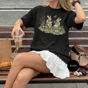 Black t-shirt with watercolor-style rabbits reading and holding flowers.