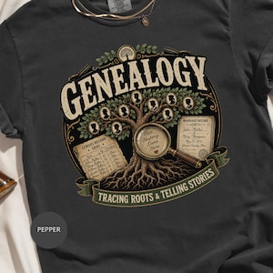 May include: A charcoal gray t-shirt featuring a graphic of a tree with silhouette portraits, a magnifying glass with the text Our History Lives Here, a 1890 census record, a marriage record, and the text Genealogy Tracing Roots & Telling Stories.