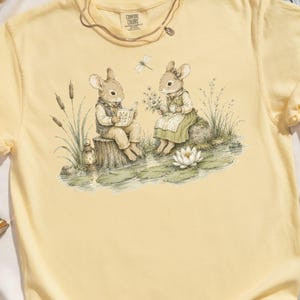 Two anthropomorphic bunnies by a pond with a book, tea, and a lantern.