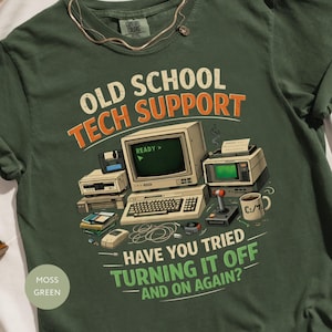 以下が含まれることがあります： モスグリーンのTシャツ。テキスト「OLD SCHOOL TECH SUPPORT」と、ヴィンテージのコンピューター機器のグラフィックが特徴です。シャツには「HAVE YOU TRIED TURNING IT OFF AND ON AGAIN？」というフレーズも表示されています。