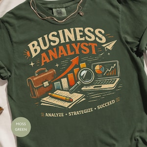 May include: Moss green t-shirt with the words "BUSINESS ANALYST" in a vintage style. The design includes a briefcase, laptop, magnifying glass, and an upward trending arrow. The shirt also has the words "ANALYZE • STRATEGIZE • SUCCEED".