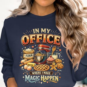 Könnte beinhalten: Marineblaues Sweatshirt mit einer farbenfrohen Grafik mit Backutensilien und Zutaten. Der Text "IN MY OFFICE WHERE I MAKE MAGIC HAPPEN" wird über den Abbildungen von Mehl, einem Mixer und Backwaren angezeigt.