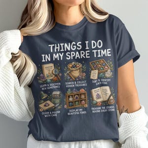 以下が含まれることがあります： 「THINGS I DO IN MY SPARE TIME」というテキストと、宝石の学習、探索、分類、洗浄、展示、記録といった収集活動を描いた6つのイラストがプリントされたダークグレーのTシャツ。