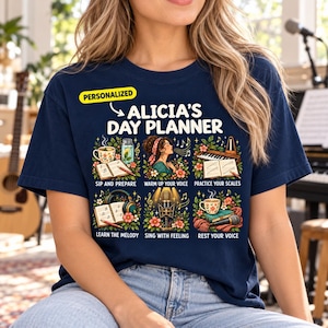 Op de afbeelding: Een marineblauw t-shirt met een afbeelding met de tekst ALICIA'S DAY PLANNER en zes geïllustreerde vierkanten met muzikale activiteiten: Sip and Prepare, Warm Up Your Voice, Practice Your Scales, Learn the Melody, Sing with Feeling en Rest Your Voice.