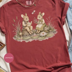 T-shirt with watercolor illustration of two anthropomorphic mice by a pond with a water lily.