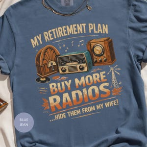 May include: Blue jean t-shirt with the text "MY RETIREMENT PLAN" and "BUY MORE RADIOS...HIDE THEM FROM MY WIFE!". The graphic features vintage radios in brown and teal.