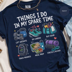 Può includere: Una t-shirt blu navy con il testo "THINGS I DO IN MY SPARE TIME" e illustrazioni colorate di attività di fitness tra cui sollevamento pesi, cardio, acquisto di attrezzatura, monitoraggio dei progressi, preparazione dei pasti e stretching.