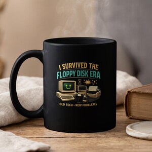 May include: A black ceramic mug featuring a graphic with the text I SURVIVED THE FLOPPY DISK ERA and OLD TECH NEW PROBLEMS. The design includes a vintage computer with a green smiley face on the screen, a dot matrix printer, and two floppy disks.