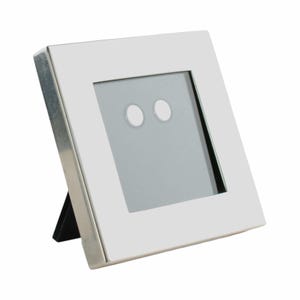 May include: A square, white picture frame with a silver metal trim. The frame has a black easel back for display. The frame's interior has a gray background with two white circles.