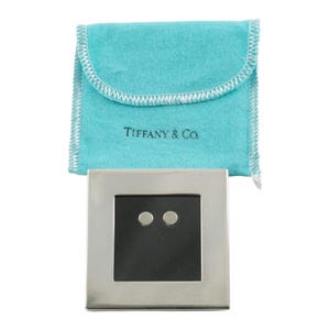 May include: A pair of silver stud earrings with a black square center, set in a silver square frame. The earrings are displayed with a light blue pouch with the text "Tiffany & Co."