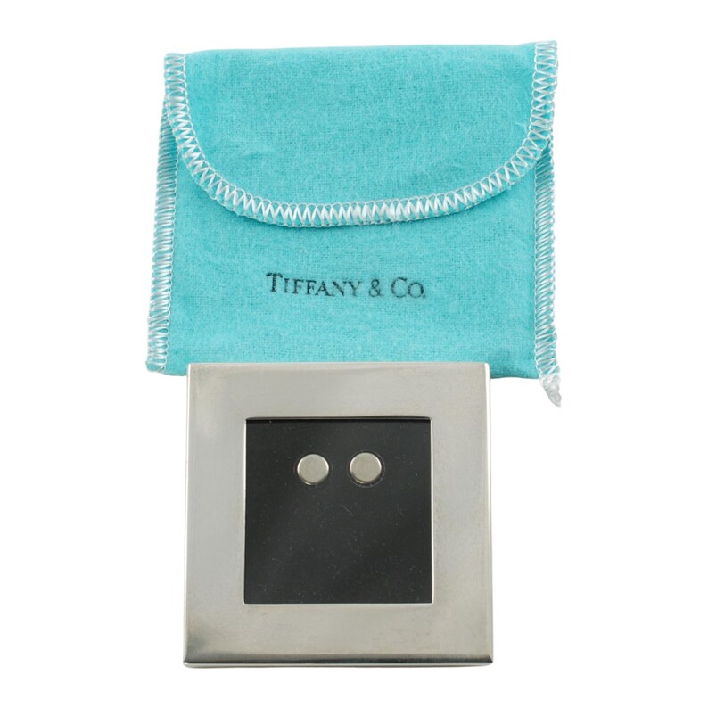 May include: A pair of silver stud earrings with a black square center, set in a silver square frame. The earrings are displayed with a light blue pouch with the text "Tiffany & Co."