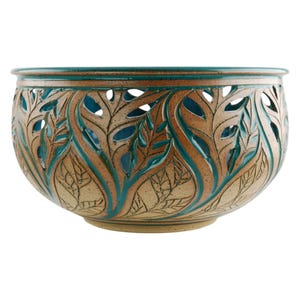 May include: A ceramic bowl with a leaf design. The bowl is tan with teal and brown accents. The leaf design is cut out around the bowl. The rim of the bowl is teal. The bowl is a decorative piece.