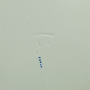 May include: Close-up of the bottom of a white ceramic plate with blue text that reads "PEACE" and "MADE IN ENGLAND".