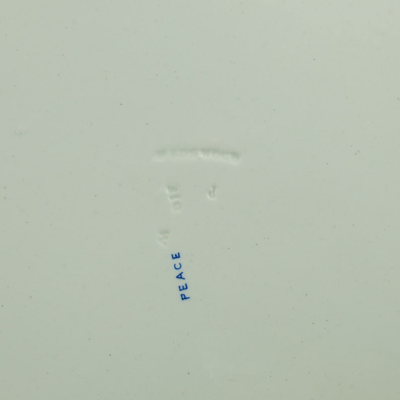 May include: Close-up of the bottom of a white ceramic plate with blue text that reads "PEACE" and "MADE IN ENGLAND".