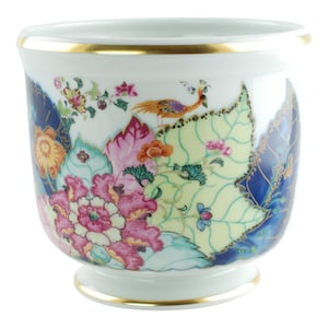 May include: A white porcelain planter featuring a vibrant floral and foliage pattern in shades of pink, yellow, green, and deep blue. The design includes a small bird perched among the leaves and flowers, finished with a gold rim and base.