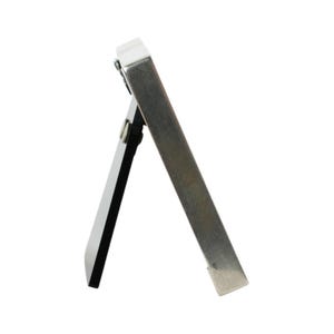 May include: A small, silver-colored easel-style picture frame with a white border and a black backing. The frame is propped up by a silver metal support on the back. The frame is designed to stand on a flat surface.