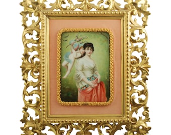 Placa antigua de porcelana pintada a mano, Doncella y Putto, "En mayo" según Foubert, con marco de madera dorada ornamentado con volutas.