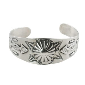 以下が含まれることがあります： 彫刻デザインのシルバーカフブレスレット。ブレスレットは、矢印と魚のようなモチーフに挟まれた、中央のサンバーストデザインが特徴です。オープンカフのデザインは、簡単に着用できます。