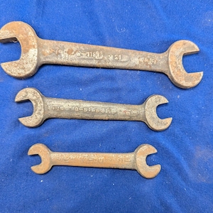 Könnte beinhalten: Drei alte Maulschlüssel mit rostigem, gealtertem Aussehen. Die Schlüssel sind aus Metall und haben an jedem Ende eine C-förmige Öffnung. Sie sind in einer Reihe angeordnet, wobei der größte Schlüssel oben und der kleinste unten ist.