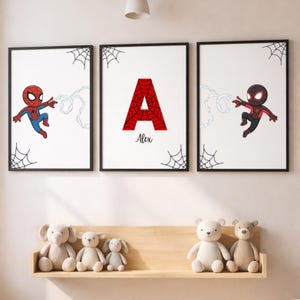 May include: Three framed art prints with Spider-Man characters and a red letter "A" with a spiderweb design. The prints are in black frames and have spiderwebs in the corners. The name "Alex" is written below the letter "A".