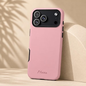 May include: A pink phone case with a black camera module and black accents. The case has the name "Maria" printed in a cursive font. The case is designed to protect a smartphone.