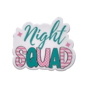 May include: A white, glittery pin with the words "Night Squad" in teal script and block letters. The word "Squad" is pink with a striped pattern. Pink diamond shapes accent the design.