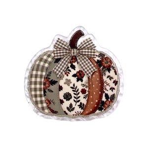 May include: A fabric pumpkin decoration featuring a patchwork design with sections of grey and white gingham, floral patterns in shades of rust, brown, and cream, and a brown stem. A small brown and white gingham bow is attached at the top.