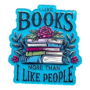 May include: A teal-colored pin with the text "I LIKE BOOKS MORE THAN I LIKE PEOPLE." The pin features a stack of books with a rose and leaves on top. The text and design are outlined in black.