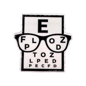 May include: A rectangular enamel pin featuring a white eye chart background with black letters. A pair of black-rimmed glasses is centered over the chart, which displays the letters E, F, L, O, Z, P, D, T, O, Z, L, P, E, D, P, E, C, F, and D.