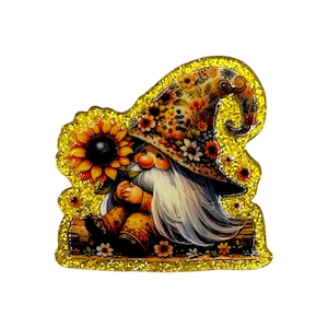 May include: A whimsical gnome figurine with a long white beard and a floral hat, holding a sunflower. The gnome is dressed in orange and brown clothing, and the entire figure is outlined with gold glitter.