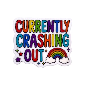 May include: A white enamel pin with the text CURRENTLY CRASHING OUT in multi-colored letters. The design includes small colorful stars and a rainbow arching over two white clouds at the bottom right, all outlined in a thin black border.