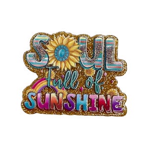 May include: A glittery, colorful pin with the words "SOUL Full of SUNSHINE". The pin features a sunflower, rainbow, and leopard print accents. The background is gold glitter.