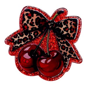 May include: A red glittery cherry-shaped brooch with a leopard print bow. The brooch features two glossy red cherries with green stems. The bow has a black and brown leopard print pattern, outlined with a silver border.