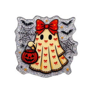 May include: A glittery enamel pin featuring a cream-colored ghost wearing a large red bow with yellow stars. The ghost is patterned with small red bows and holds an orange jack-o'-lantern bucket. The background includes black spiderwebs, spiders, and bats.