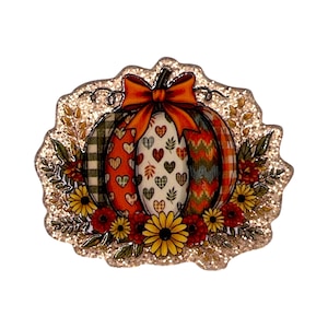 May include: A decorative pumpkin-shaped ornament with a glittery finish, featuring vertical segments with plaid, heart, and chevron patterns in orange, green, and white. An orange bow sits at the top, surrounded by yellow and red floral accents.