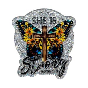 May include: A glittery, butterfly-shaped pin with a cross in the center. The butterfly wings feature a floral design with yellow and blue accents. The words "SHE IS STRONG" and "PROVERBS 31:25" are written on the pin.