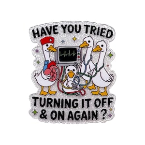 May include: A glittery enamel pin featuring three white ducks dressed as medical staff with stethoscopes and a red nurse cap. One duck holds a red heart. A medical monitor displays a heartbeat. The text reads: HAVE YOU TRIED TURNING IT OFF & ON AGAIN?